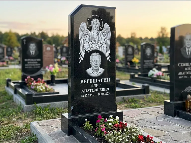 Памятник с гравировкой иконы: стела с резным навершием и нимбом в золоте — гравировка образа Спасителя, высокие разросшиеся туи полукругом, работа «Мельникова» в Иркутске