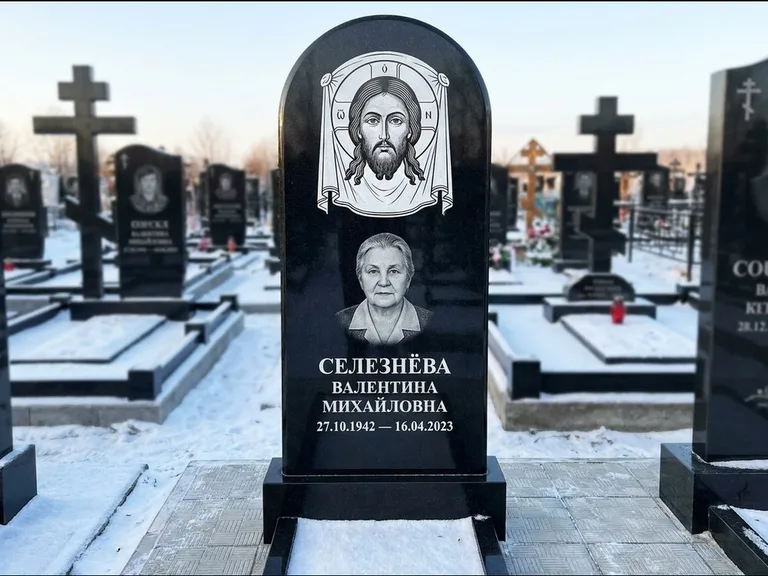 Памятник с гравировкой иконы: небольшая скромная одиночная стела с именной иконой — золочёный нимб на образе, аккуратный участок с газоном, работа «Ковалёв» в Иркутске