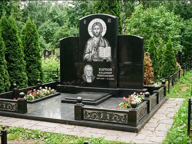 Памятник с гравировкой иконы: широкая панорамная стела с золочёным нимбом — гравировка образа Матроны Московской, цветник с белыми хризантемами, работа «Мельникова» в Иркутске