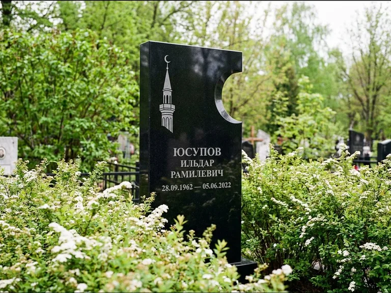 Мусульманский памятник с гравировкой мечети: стела с боковым вырезом в форме полумесяца — гравировка минарета с полумесяцем, низкие кусты спиреи в цвету, работа «Юсупов» в Иркутске